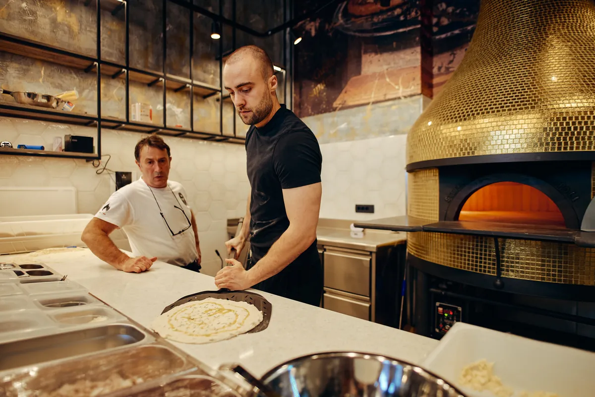 Kuhinja: dva kuharja, zlata peč, pult, pica v pripravi.